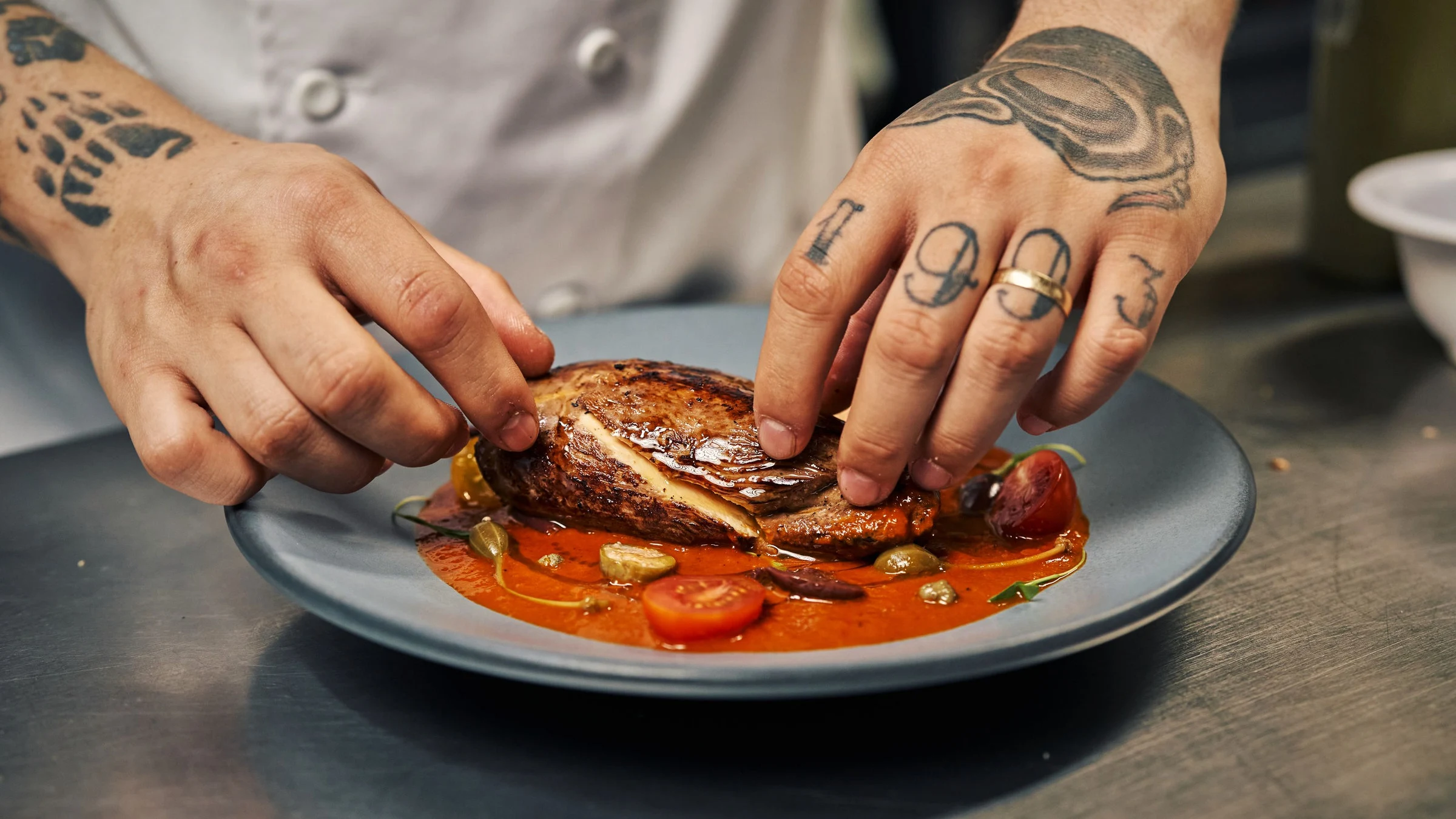 Fotografía de referencia: las manos de un cocinero terminan el montaje de un platillo en la cocina.