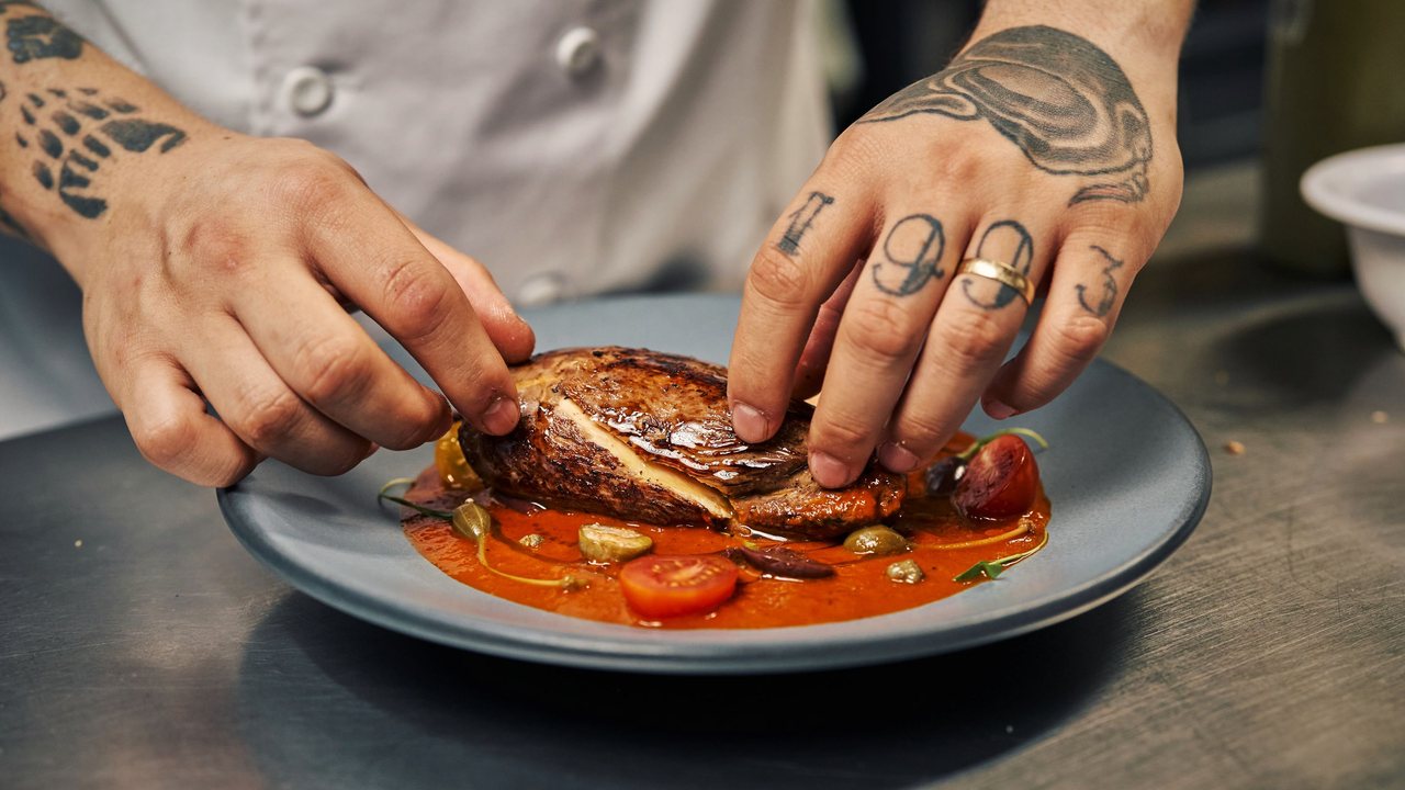 Fotografía de referencia: las manos de un cocinero terminan el montaje de un platillo en la cocina.