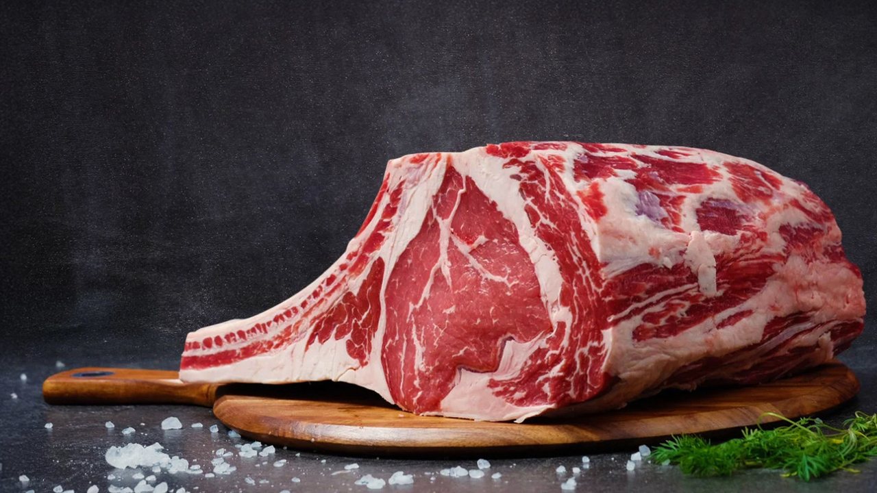Fotografía de referencia: pieza de costilla de res cruda y marmoleada sobre una tabla de madera, con sal gruesa.