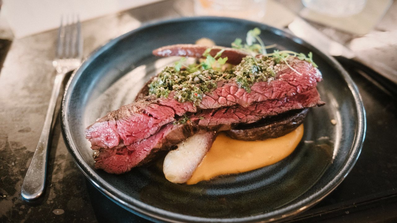 Fotografía de referencia: corte de res término medio con chimichurri, puré y hongo en un plato oscuro.