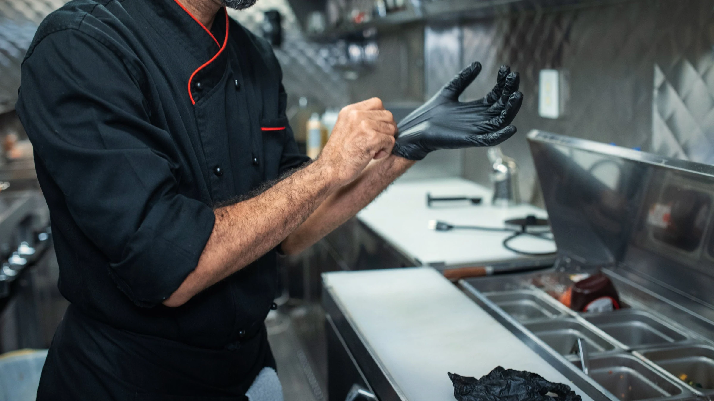 Fotografía de referencia: un cocinero se pone guantes desechables en una cocina profesional de acero inoxidable.