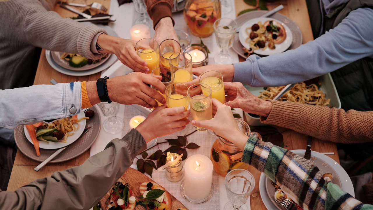Fotografía de referencia: las manos de varias personas brindan sobre una mesa llena de platillos y velas.