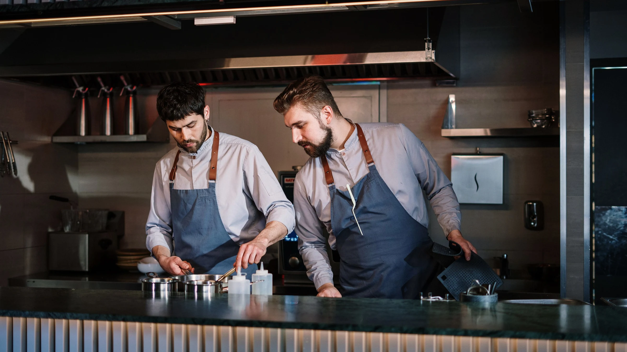 Fotografía de referencia: dos cocineros trabajan juntos en una cocina abierta.