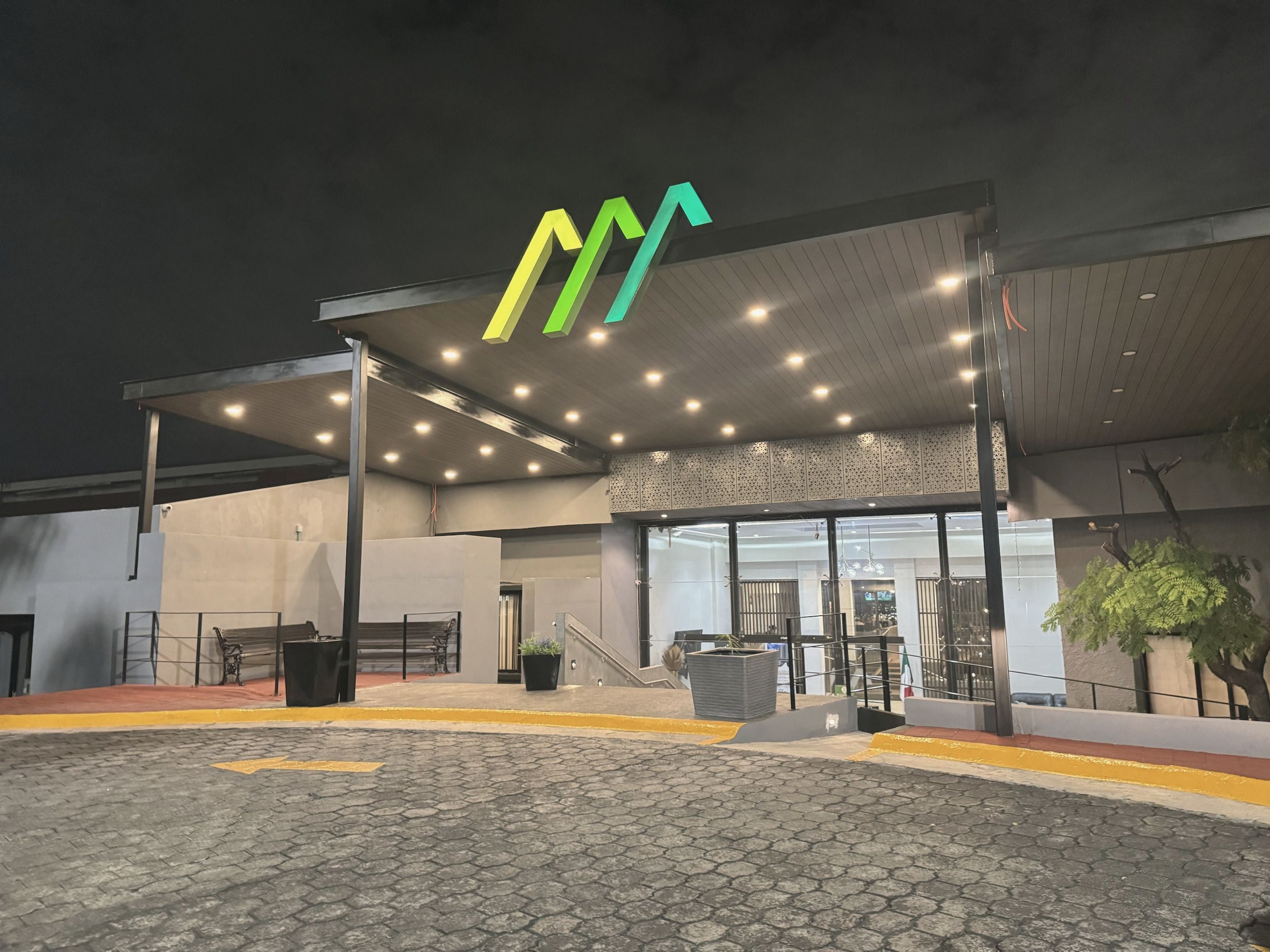Entrada principal del club de noche, con la marquesina iluminada y el logotipo del club encendido en verde.
