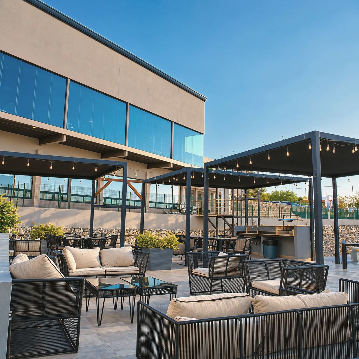 Terraza al aire libre con salas de exterior, pérgolas y focos colgantes junto al edificio del club.